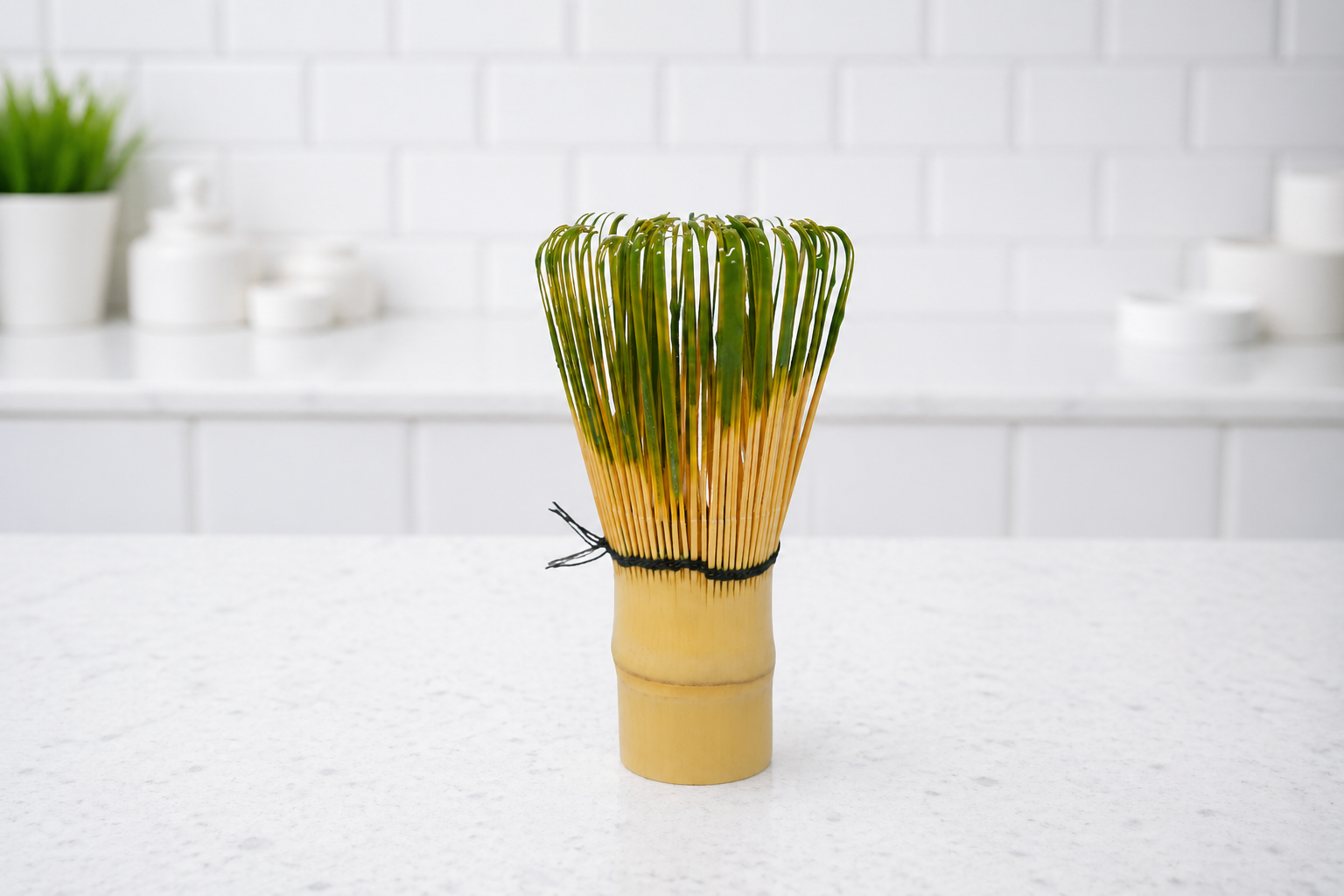 Bamboo whisk with green bristles on a white surface